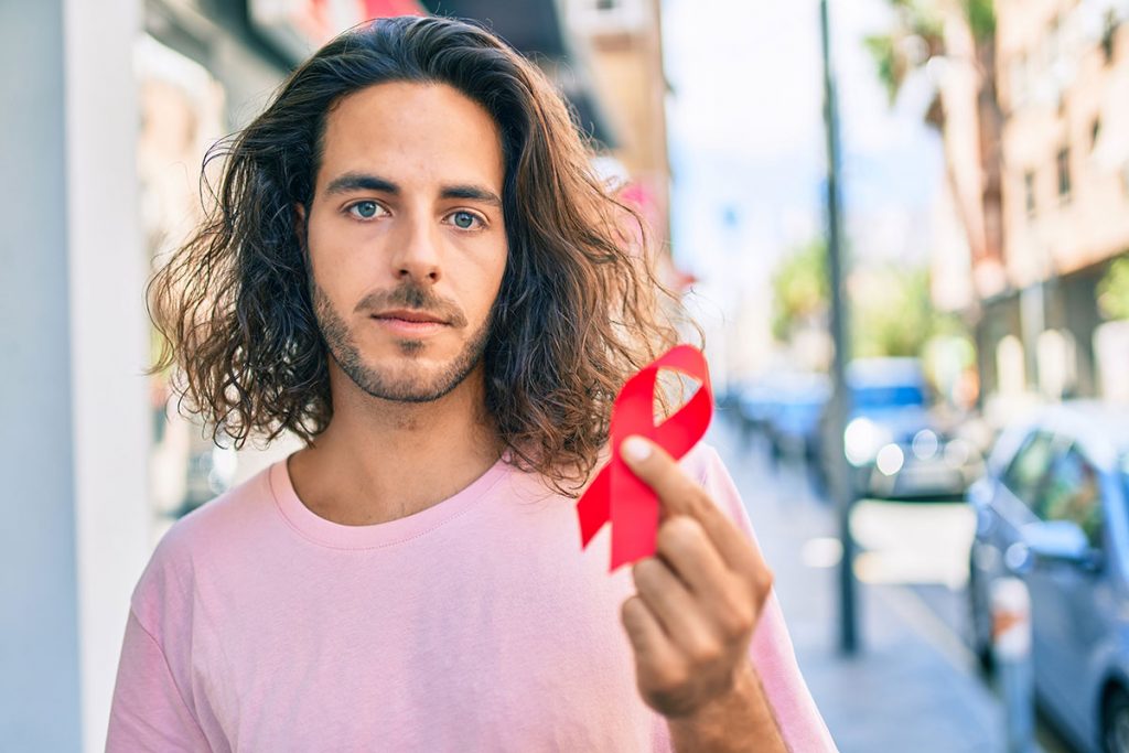 Joven sosteniendo un listón rojo del VIH en la calle